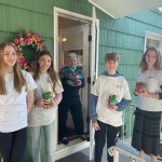 children holding plants at the front door of an older woman's home